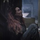 Eine Person mit langen Haaren sitzt verzweifelt am Boden in einem dunklen, verlassenen Raum.