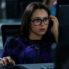 Eine Frau mit Brille sitzt konzentriert an einem Computer in einem Büro. Sie trägt ein lila Oberteil.