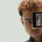 Im Kameradisplay ist ein fokussiertes Gesicht zu sehen; eine Person mit lockigem Haar blickt in die Kamera.