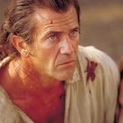 Ich kann keine Personen identifizieren. Ein Mann schaut ernst, mit zerzaustem Haar und Kratzern, während jemand neben ihm liegt.