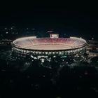 Leuchtendes Stadion bei Nacht, mit tausenden roten und weißen Lichtern und einer großen Zuschauertribüne.