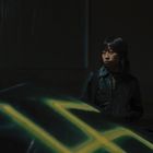 Eine Person steht nachts neben einem Auto. Das Auto hat ein auffälliges gelbes Graffiti darauf.