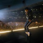 Links steht "Michael Jackson". Ein Künstler, in schwarzem Outfit, performt auf einer Bühne vor einem großen Publikum.