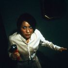 Eine Person in weißem Hemd hält eine rote Taschenlampe, schaut ängstlich, umgeben von Dunkelheit.