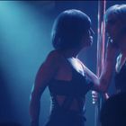 Zwei Personen mit kurzen Haaren, in dunkler Kleidung, stehen nah beieinander neben einer Stange im blauen Bühnenlicht.