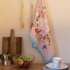 Text "hier blüht das leben" auf einem floralen Küchentuch, daneben Holzbrett, Obstschale und Tasse auf Tisch.