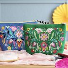 Zwei bunte Kosmetiktaschen mit floralen Stickmustern in lebhaften Farben auf grünem und blauem Stoff.