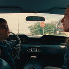 Text „STOP“ auf einem Verkehrsschild. Zwei Personen sitzen lächelnd in einem Auto und unterhalten sich.