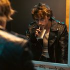 Der Text im Bild lautet: "LOVE," "dream BIG," und "smile often." Ein Mann in Lederjacke blickt ernst in den Spiegel.