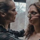 Zwei Frauen stehen sich nahe. Die jüngere trägt eine viktorianische Atemmaske. Sie schauen sich intensiv an.