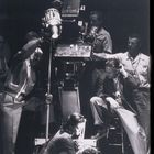 Eine Filmszene: Eine Frau hält eine liegende Person, umgeben von einer Filmcrew mit Kamera und Scheinwerfer.