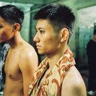 Zwei junge Männer mit kurzen, nassen Haaren stehen in einem Umkleideraum, mit Handtüchern um die Schultern.