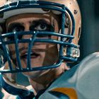 Ein Footballspieler mit Helm, blauem Gitter und Augenstreifen, fokussiert mit entschlossenem Ausdruck auf das Geschehen.