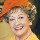 Person mit orangefarbener Kappe, gelbem Oberteil und Kette, lächelt. Die Kappe hat den Text "Dolle" aufgedruckt.