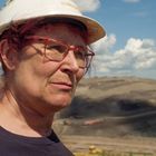 Eine Person mit Helm und Brille blickt ernst in die Ferne, im Hintergrund eine weite, wolkige Landschaft.