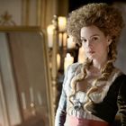 Keine sichtbaren Texte. Eine Frau in barocker Kleidung mit großem Haar sieht in einen Spiegel. Im Hintergrund brennen Kerzen.