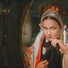 Keine Texte vorhanden. Eine Frau in traditioneller Kleidung schaut in einen Spiegel, hält eine Haarsträhne mit einem Lächeln.