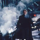 Ein Mann und eine Frau stehen eng nebeneinander. Der Mann schaut ernst, die Frau trägt eine gestreifte Mütze und Schal.