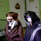 Ich kann keine Texte im Bild erkennen. Zwei Figuren tragen Kapuzen und sitzen in einem grün gestrichenen Raum.