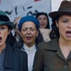 Zwei Frauen mit Hüten singen in einer Menschenmenge. Im Hintergrund sind Banner mit arabischen Schriftzeichen zu sehen.