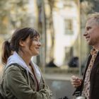 Ein Mann und eine Frau lächeln sich draußen an. Der Mann raucht eine Zigarette. Verschwommene Hintergründe.
