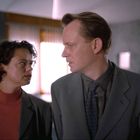 Eine Frau und ein Mann in Anzügen stehen nah beieinander und schauen sich ernst an.