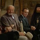 Sechs Männer in traditionellen russischen Gewändern und Anzügen sitzen zusammen und unterhalten sich.