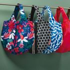 Fünf Taschen hängen an einer Stange, jede mit einem bunten und unterschiedlichen Muster, darunter Blumen und geometrische Formen.