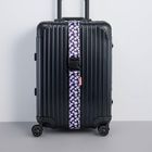 Text "RIMOWA" an der Seite eines schwarzen Koffers mit einer lilafarbenen Blumenbanderole und Rollen.