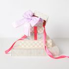 Stapel von Geschenkschachteln in neutralen Tönen mit rosa und lila Schleifen.