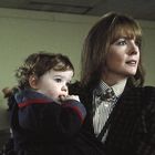 Eine Frau hält ein kleines Kind auf dem Arm. Sie schauen aufmerksam zur Seite. Im Hintergrund sind gerahmte Bilder.