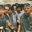 Viele Männer in grauen Hemden schauen ernst, zwei tragen Stirnbänder.