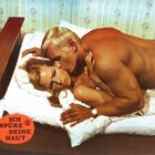 Text: "ICH SPÜRE DEINE HAUT". Ein Mann umarmt eine Frau in einem Bett. Die Szene wirkt intim und in einem Schlafzimmer.