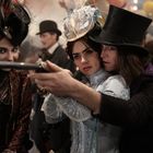 Persönlichkeiten in viktorianischer Kleidung. Eine Frau zielt mit einem Gewehr, assistiert von einem Mann im Zylinder.