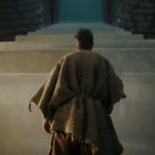 Eine Person in grobem Gewand steht vor einer großen Treppe, die in die Höhe führt.