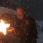 "SHERIFF DEPARTMENT" steht auf einer Uniform. Ein Mann schießt in dichter Schneelandschaft. Es ist dunkel und schneit stark.
