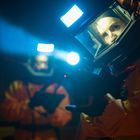 Zwei Personen in Schutzanzügen mit beleuchteten Helmen, eine mit einem Gerät, das Lichtstrahlen sendet.