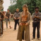 Eine Gruppe von sieben Menschen steht in Westernkleidung in einer Wildwest-Kulisse aus Felsen und Bäumen.