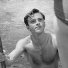 Ein Mann hält sich an einer Poolleiter fest und schaut lächelnd nach oben. Im Vordergrund ist ein Bein zu sehen.