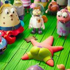 Im Zentrum liegt ein Seestern ähnlich einer Figur. Um ihn herum stehen bunte Figuren auf einem grünen Boden.