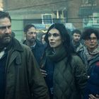 Ich sehe keine spezifischen Texte. Eine Gruppe von Menschen blickt besorgt in dieselbe Richtung. Dämmerige, urbane Umgebung.