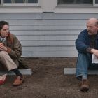 Eine Frau und ein Mann sitzen draußen auf Betonkanten. Die Frau isst, während der Mann ein Papier hält.