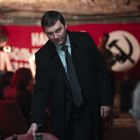 „Russland bleibt unbesiegt“ steht auf einem roten Banner mit Hammer-und-Sichel-Symbol. Ein Mann im Anzug ist im Vordergrund.