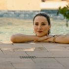 Eine Frau lehnt sich entspannt an den Beckenrand eines Pools, mit Schmuck an den Handgelenken.