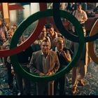 Eine Gruppe von Menschen blickt fasziniert auf die Olympischen Ringe, die prominent im Vordergrund hängen.