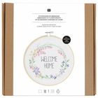 „Welcome Home“ in Blumenstickerei in einem Ring, Anleitung in drei Sprachen. Ringdurchmesser 20 cm.