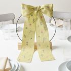 Ein großer, gelber Stoffbogen mit floralen Mustern steht auf einem gedeckten Tisch mit Tellern und Gläsern.