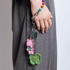 Ein pinkes Bärchen-Anhänger, grüner Schlüssel, bunte Perlenkette, an der Hand einer Person mit grauer Kleidung.