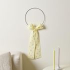 Ein gelbes Tuch mit Blumendruck hängt an einem Ring an der Wand. Daneben stehen zwei gedrehte Kerzen und ein Espresso auf einem Tisch.