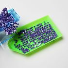 Kleine lila Glitzersteine auf einem grünen Tablett, einige fallen aus einer blauen Verpackung heraus.